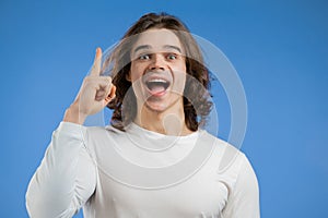 Young thinking pondering man having idea moment pointing finger up on blue studio background. Smiling happy guy showing