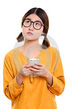 Young thoughtful Asian woman holding mobile phone