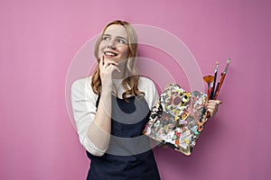 Young thoughtful girl artist thinks and dreams on a pink background and looks at a place for text, the girl has an idea