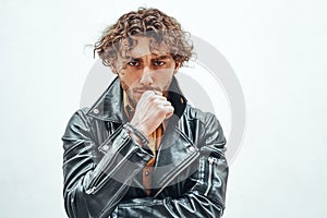 Young and and thoughtful male model with curly hair posing in a studio wearing leather jacket