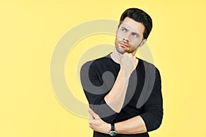 Young thoughtful man thinking and looking aside on copy space isolated on yellow background