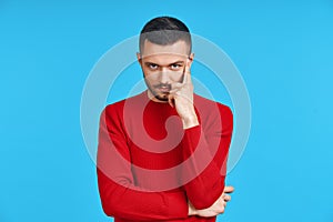 Young thoughtful man thinking and looking to camera with copy space, isolated on blue background