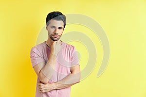 Young thoughtful man thinking and looking to camera with copy space, isolated on yellow background