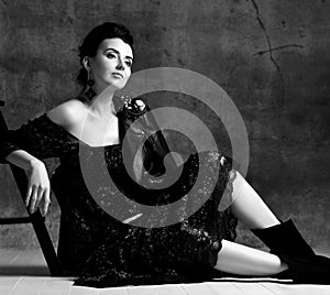 Portrait of young beautiful dreamy pregnant woman in black lace dress and leather jacket sitting on floor and looking up