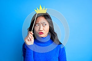 Young thoughtful woman with paper crown on stick looking away expressing doubt