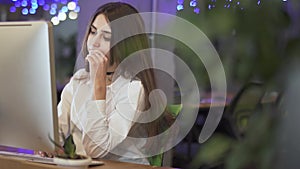 Young thoughtful woman sitting at her workplace in front of modern computer in the office typing on keyboard. Background