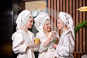 Young three women drinking juicy detox juice beverage after spa treatment, having rest, enjoying beauty procedures