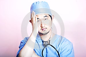 Young tired Asian surgeon wearing scrubs and looking stressed