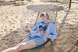 Young tired businessman lies on a chaise longue in a shirt with a tie and boxer shorts. Rest at sea, reboot