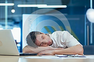 Young tired businessman sleeping on the desk at workplace in the office