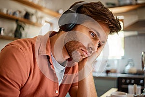 Young tired caucasian businessman wearing headphones and listening to music while working from home alone. One stressed