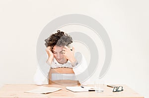 Young, tired Caucasian freelancer man sitting in his home office at the table in front of empty clear wall.
