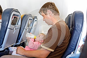 Young tired father carry his baby daughter during flight on airplane.