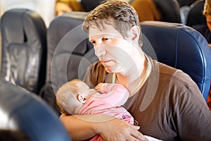 Young tired father and his baby daughter sleeping during flight on airplane going on vacations. Dad holding baby girl on