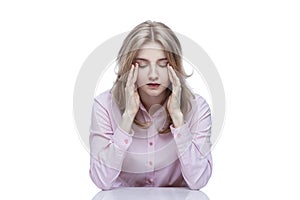 A young tired girl sits at a table and puts her hands on her head. Cute blonde girl in a pink shirt Work, study and stress.