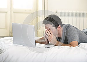 Young tired man lying on bed or couch working on computer laptop at home wireless connected to internet in technology concept