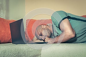 Young tired man taking a break and fell asleep on the bed with his lap top computer after hard and long online work, dark image