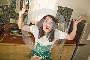Young tired and stressed Asian Korean woman in cook apron working in the kitchen screaming desperate and pulling her hair