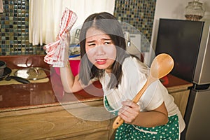 Young tired and stressed Asian Korean woman in cook apron working leaning on kitchen sink lazy in moody and upset face