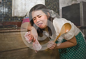 Young tired and stressed Asian Korean woman in cook apron working leaning on kitchen sink lazy in moody and upset face