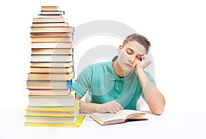Young tired student sitting at the desk with high books stack
