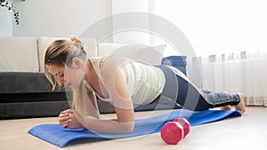 Young tired woman doing plank exercise on fitness mat at home