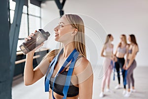 Young tired woman drinking water after hard group fitness training