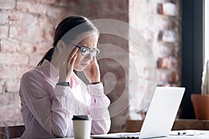 Young tired woman in eyeglasses working at office