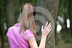 Young tired woman resting leaning to tree trunk in summer forest