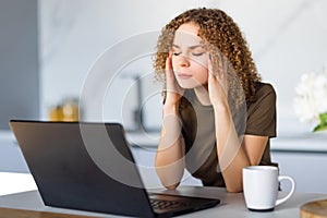 Young tired woman sitting in front of laptop while touching her forehead during work over project