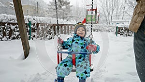 Young toddler boy smiling as he swings in the snow-covered park on a cold winter day. Perfect for conveying the joy and magic of
