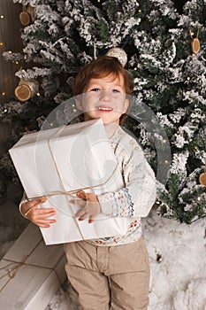 Young toddler Caucasian Boy Holding Christmas Present In Front Of Christmas Tree. Cute happy smiling boy. Vertical photo