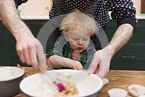 A young toddler having fun helping his dad bake cakes in the kitchen..