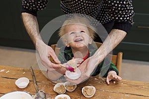 A young toddler having fun helping his dad bake cakes in the kitchen.