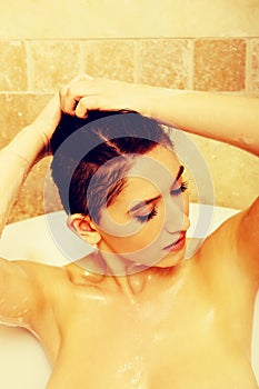 Young topless woman washing hair in bath