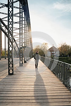 Young tourist with a backpack walking alone on a wooden bridge during the sunset