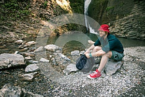 Young tourist camping with backpack near a waterfall in forest.