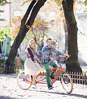 Young tourist couple, handsome man and pretty blond woman riding tandem bicycle along city street.