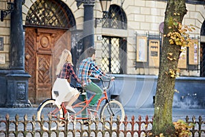 Young tourist couple, handsome man and pretty blond woman riding tandem bicycle along city street.