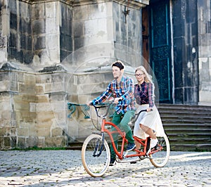 Young tourist couple, handsome man and pretty blond woman riding tandem bicycle along city street.