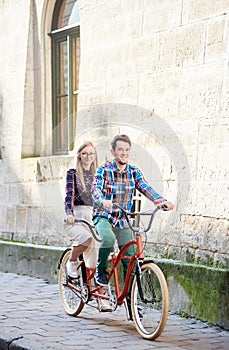 Young tourist couple, handsome man and pretty blond woman riding tandem bicycle along city street.