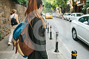 A young tourist girl with a backpack in the big city is waiting for a taxi. Journey. Sightseeing. Travel.