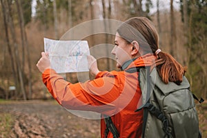 young tourist girl in sports clothes with a map in her hands shows the directions of the path in the autumn forest