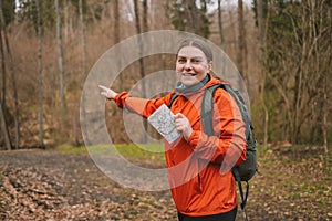 young tourist girl in sports clothes with a map in her hands shows the directions of the path in the autumn forest