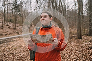 young tourist girl in sports clothes with a map in her hands shows the directions of the path in the autumn forest