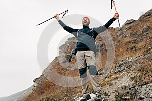 Young tourist male hiking in mountains, finished his track, feels happy. Traveler bearded man mountaineering during his journey