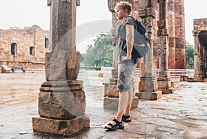 Young tourist man waits when intense rain stop on the yard of Qutb Minar Komplex in India, New Delhi