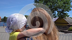 Young tourist mother carries a tired baby boy near lake. Gimbal back follow