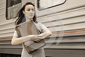 A young tourist in retro style hugs her vintage suitcase