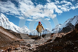 Young tourist walk along high altitude track among snowy and cloudy mountains. Man expeditor with travel backpack going across